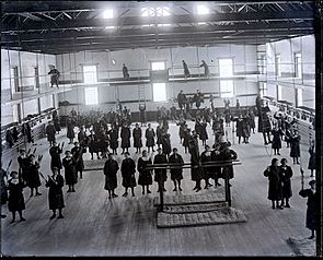 Archivo:Group of Young Women Students in School Uniform at Gym Class; Some with Indian Clubs; Some on Parallel Bars, Others on Catwalk Above Gym Floor 1880