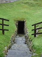 Entrada al pozo con cámara de Burghead, en el lado de una colina cubierta de hierba.