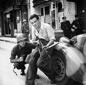 Archivo:American officer and French partisan crouch behind an auto during a street fight in a French city. - NARA - 531322 - restored by Buidhe