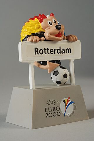 Officiële mascotte van Euro 2000, leeuw achter plaatsnaambord Rotterdam, tweedelig, leeuw hangt los aan het bord, objectnr 78426-A-B.JPG