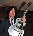Tommy Thayer without KISS makeup, holding up autographed guitar, 2013