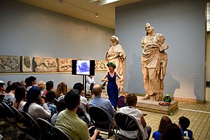 Archivo:An actress performs a play in front of 2 statues from the Mausoleum at Halicarnassus. Room 21, the British Museum, London