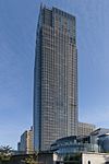 Ground-level view of a rectangular, glass high-rise; a smaller, circular building is in the foreground