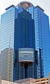Ground-level view of a blue, glass high-rise; a circular pad sits atop the structure