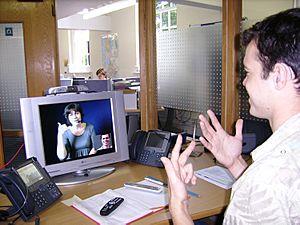 Archivo:Deaf or HoH person at his workplace using a Video Relay Service to communicate with a hearing person via a Video Interpreter and sign language SVCC 2007 Brigitte SLI + Mark
