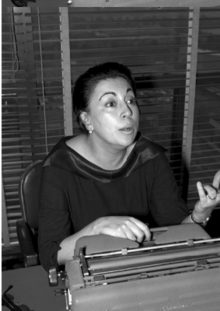 Rosario Castellanos conversa sentada tras un escritorio, retrato.png