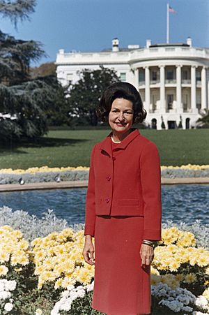 Archivo:Lady Bird Johnson, photo portrait, standing at rear of White House, color