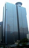 Ground-level view of a blue, glass, rectangular high-rise lined with rows of windows; a small circular pad sits atop the building