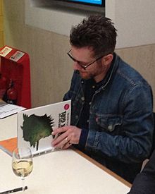 Jamie Hewlett in 2014 signing copies of "The Cream of Tank Girl" at a Tank Girl lecture at the British Library- 2014-07-03 08-13.jpg