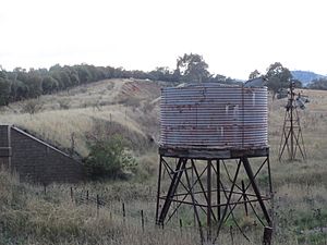 Archivo:Derelict windpump with water tank in the foreground next to the Boorowa railway in Galong NSW Australia