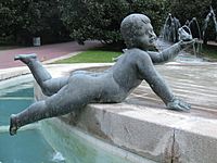 Imagen de un angelote en piedra, tumbado sobre su vientre en el borde de una fuente