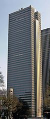 Ground-level view of a brown, rectangular high-rise with rows of black windows; one side is vertically bisected