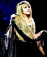 Stevie Nicks aparece en el escenario sosteniendo un micrófono y mirando a su izquierda.