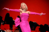 Monroe en Los caballeros las prefieren rubias. Lleva un vestido rosa impactante con guantes a juego y joyas de diamantes, y está rodeada de hombres con esmoquin.